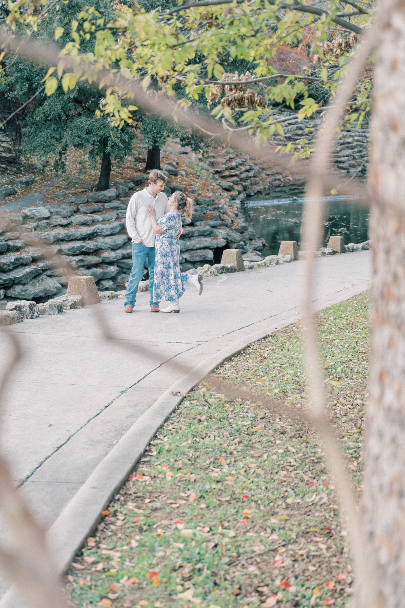 A couple shares a tender moment on stone steps surrounded by autumn foliage in a park setting.