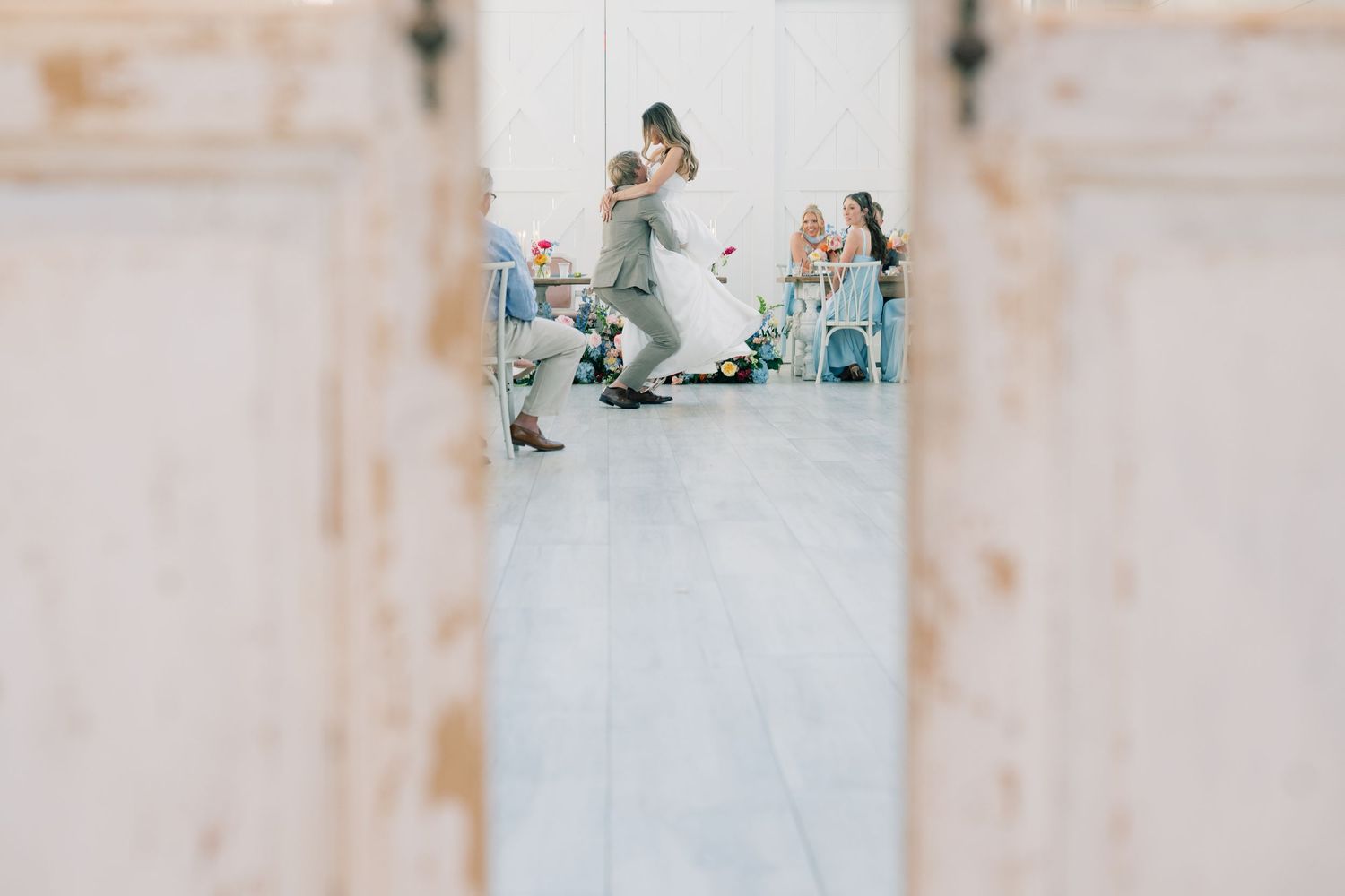 Couple sharing first dance at elegant wedding reception viewed through rustic white barn doors.