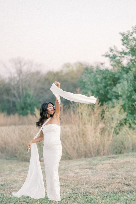 Graceful pose with flowing white fabric against natural backdrop of trees and tall grass.
