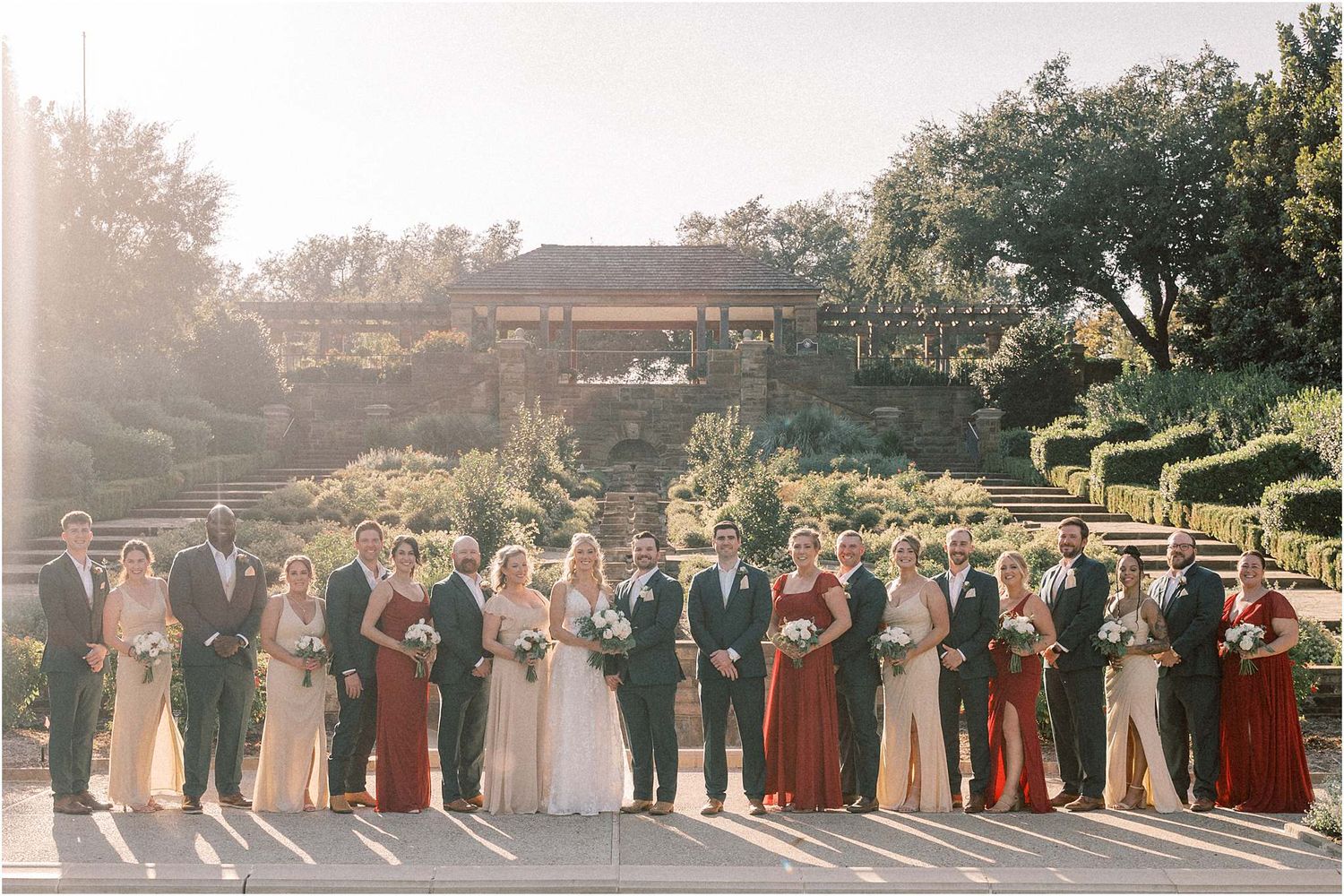 Large wedding party lines up for a panoramic group photo during golden hour.