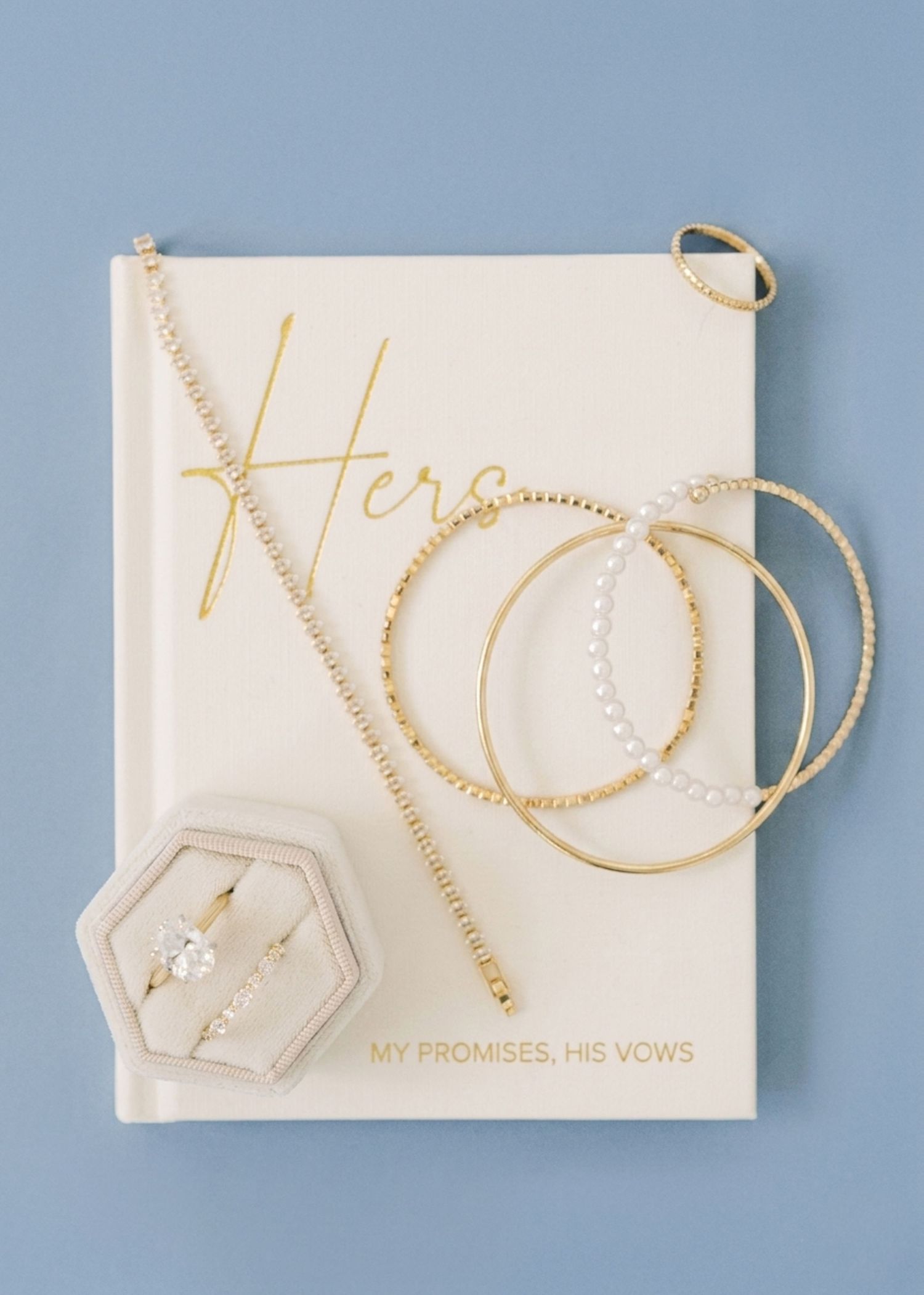 Gold bridal jewelry set with hoop earrings, pearl bracelets, diamond ring in box, on a Her vows book.