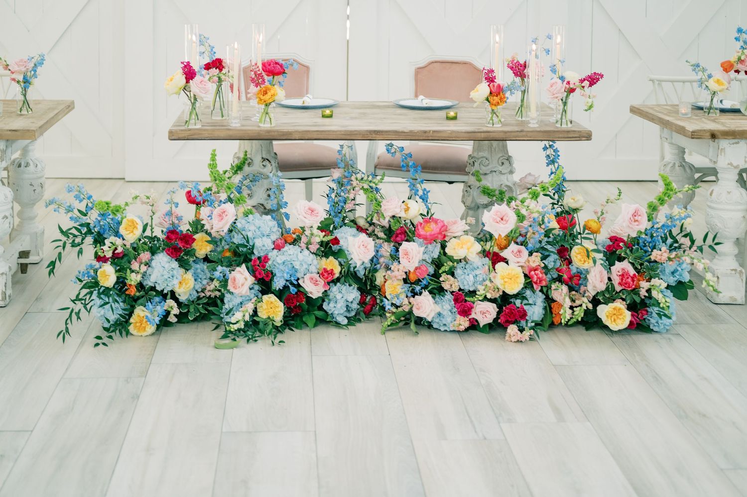 Colorful floral arrangement with pink, blue, and yellow blooms decorating a elegant wedding reception table.