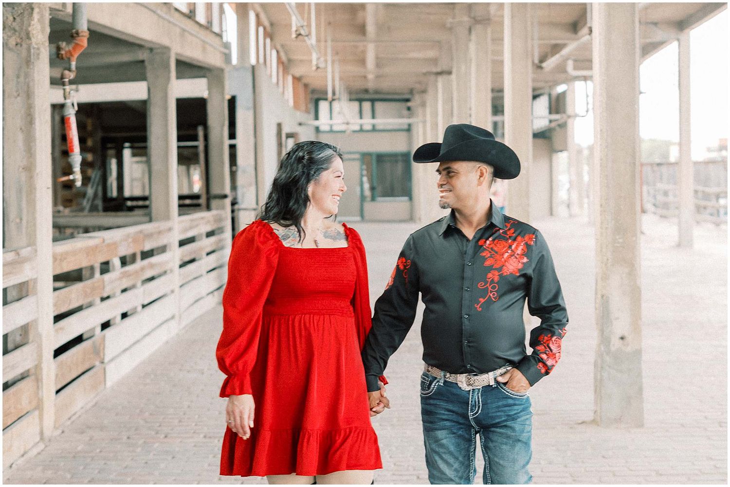 Two people in contrasting outfits share tender moments along a bright concrete corridor.