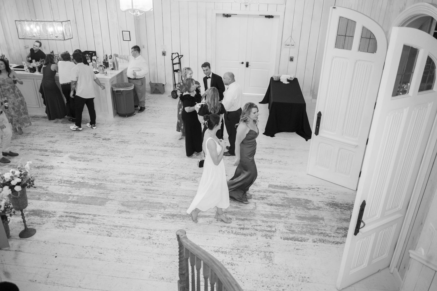 Aerial black and white photo of wedding guests dancing on a white hardwood floor inside an elegant reception venue.