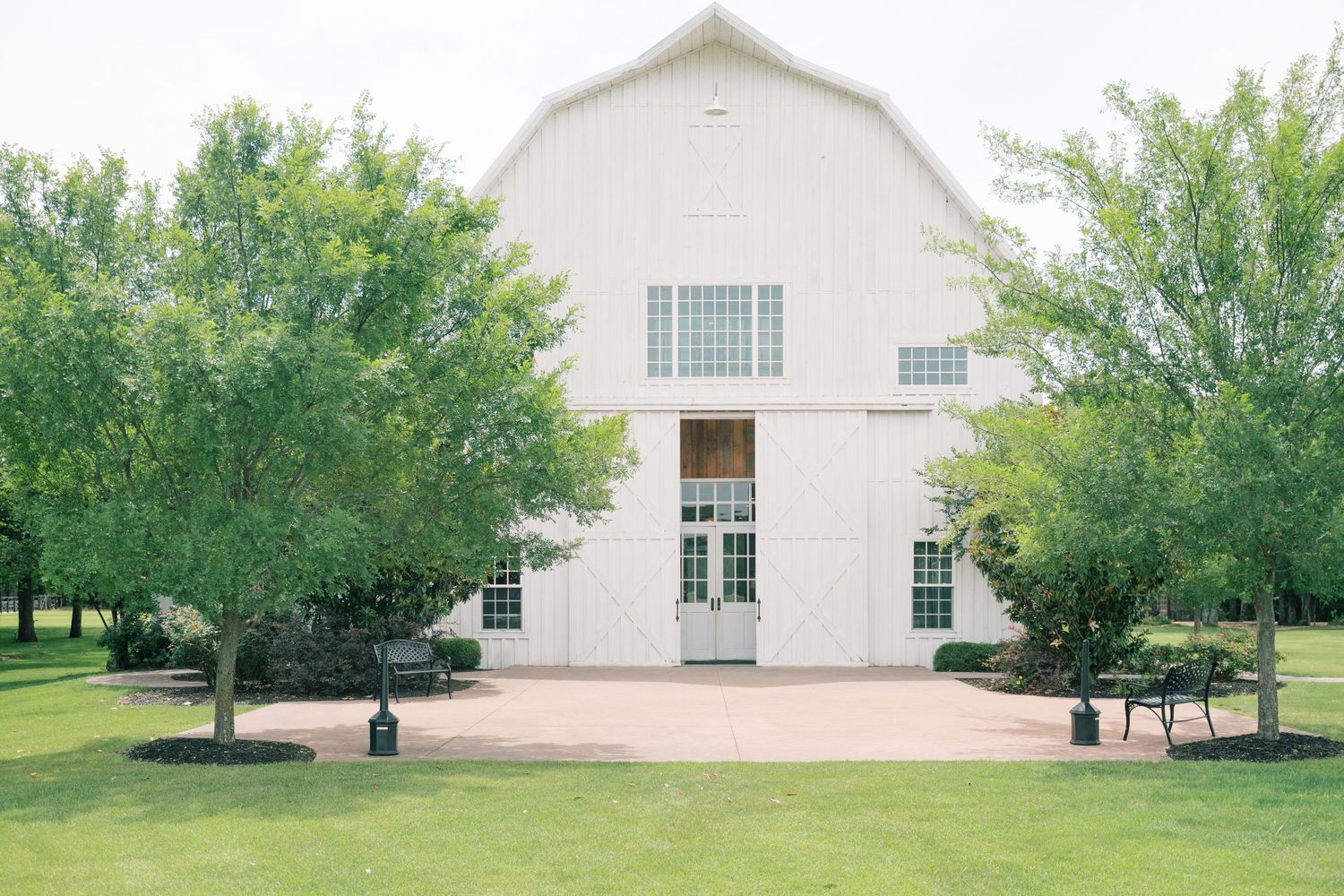 Elegant white barn wedding venue surrounded by green trees on sunny day.