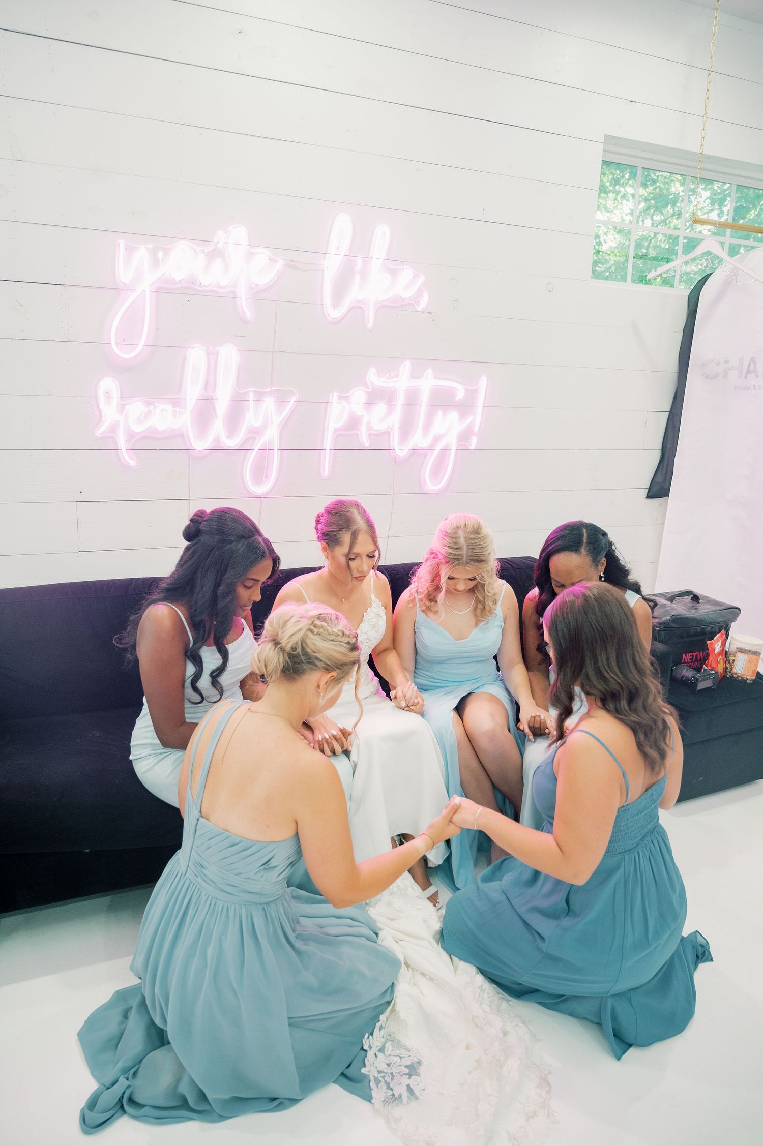 Wedding party in blue dresses sits together under pink neon lighting at reception.