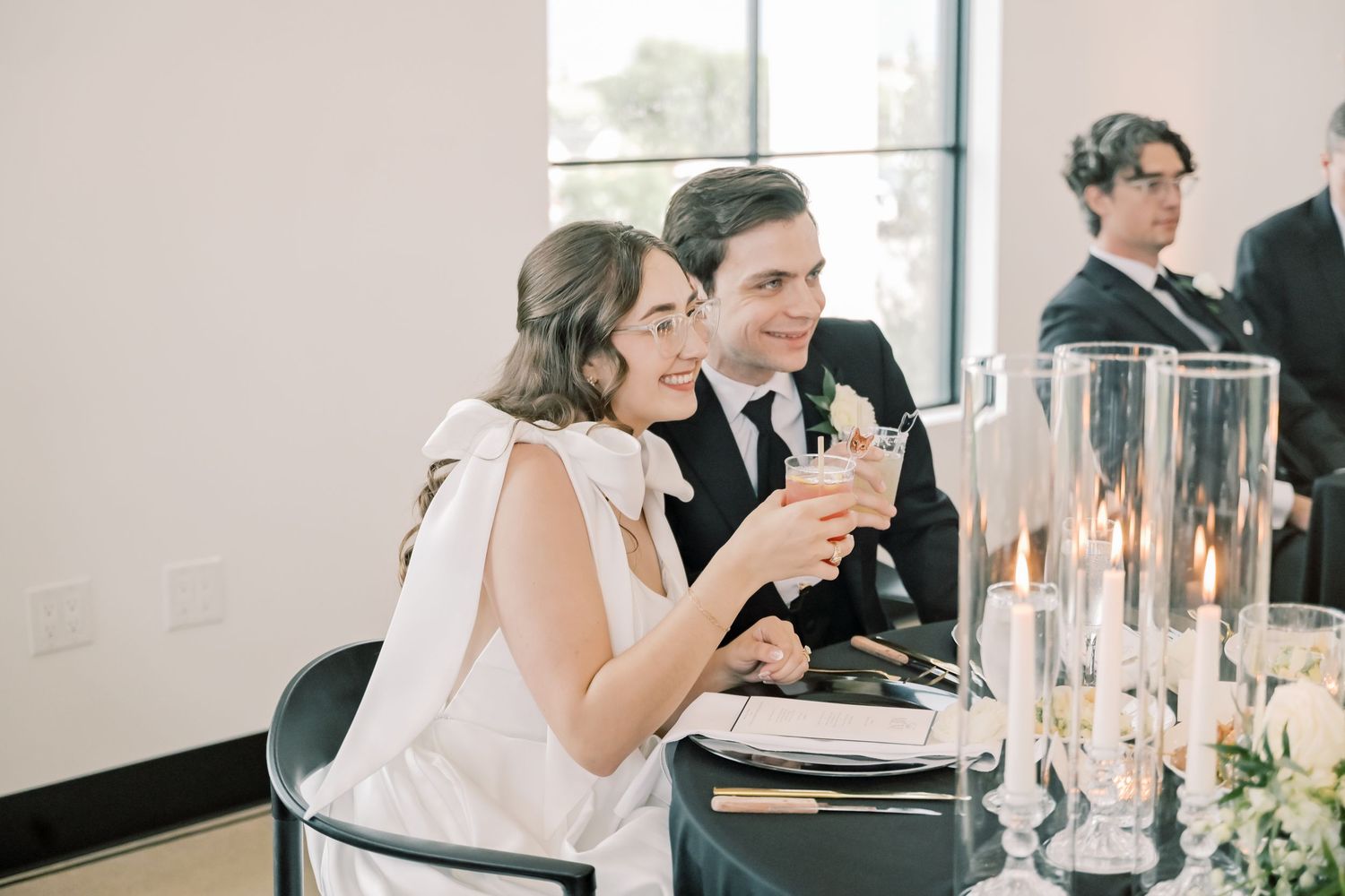 Bride and groom smile and toast at their elegant candlelit wedding reception table.