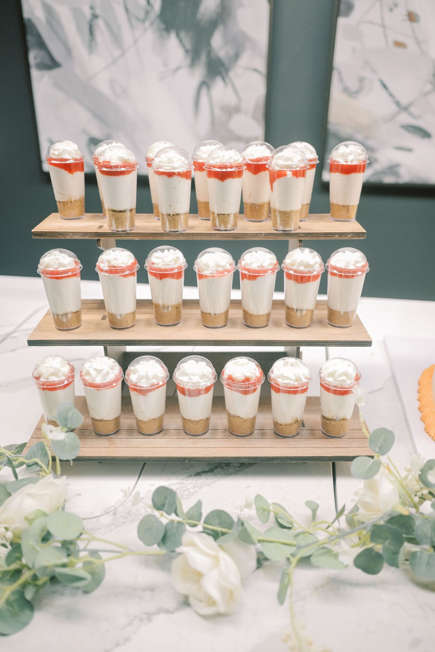 Three-tiered wooden display holds strawberry cheesecake dessert cups at a wedding reception.