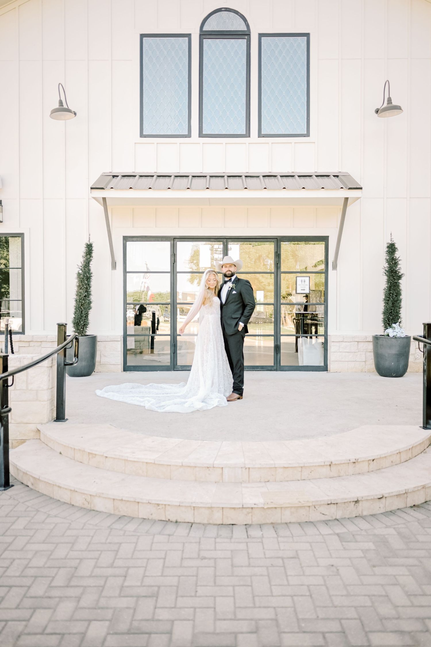 Bride and groom share romantic moment on steps of elegant white barn wedding venue entrance.