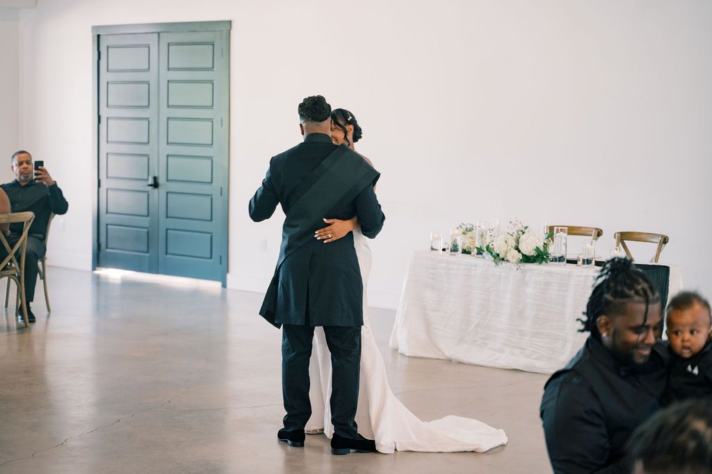Bride and groom share an intimate first dance embrace near teal doors in an elegant white reception hall.
