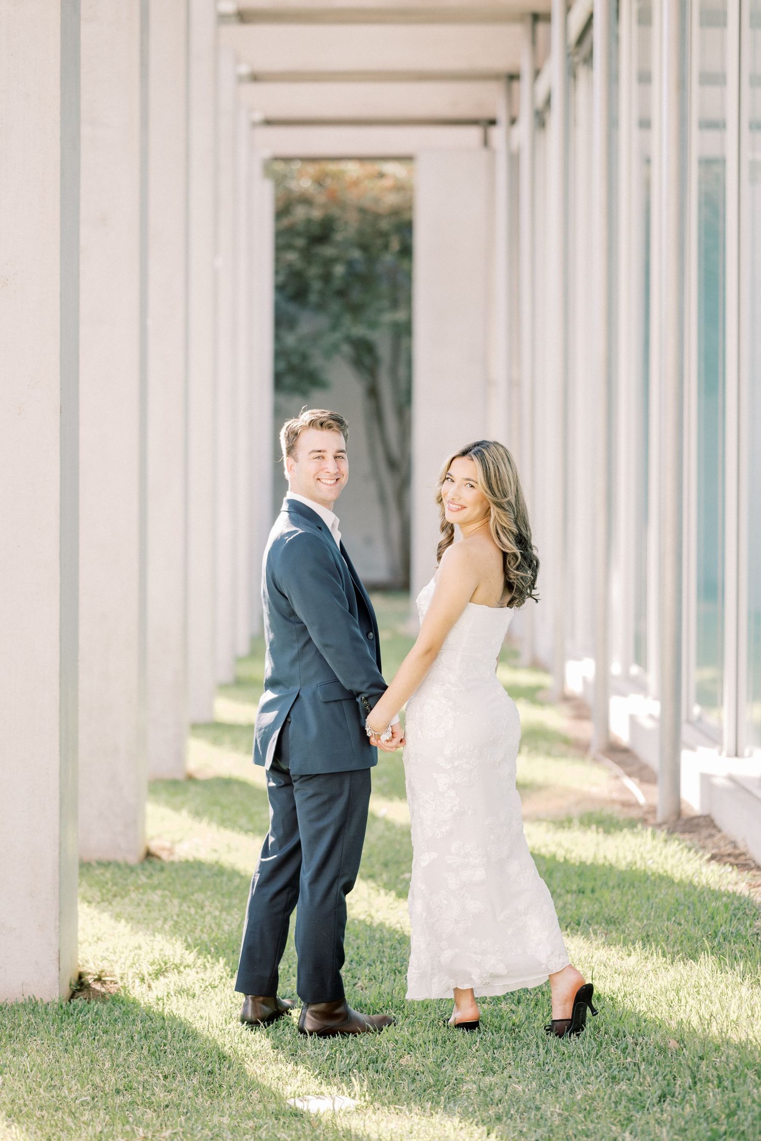 Newlywed couple playfully peeks around white columns in a romantic outdoor wedding photo session.