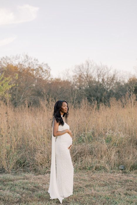A woman in a flowing white dress poses gracefully in a golden autumn field with trees in the background.
