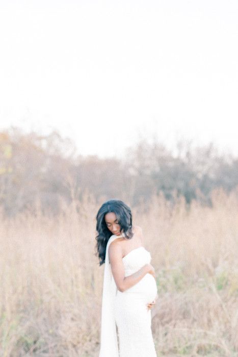 A person in a white dress poses in a natural field setting during golden hour.