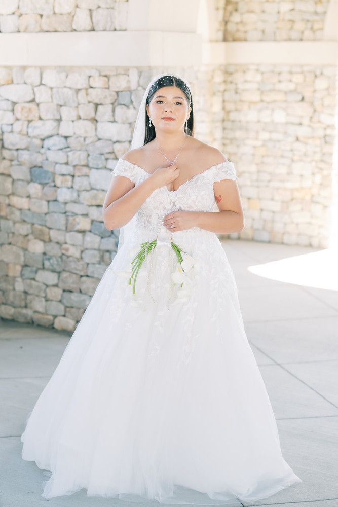 Bride in flowing white ball gown stands gracefully against stone architecture.