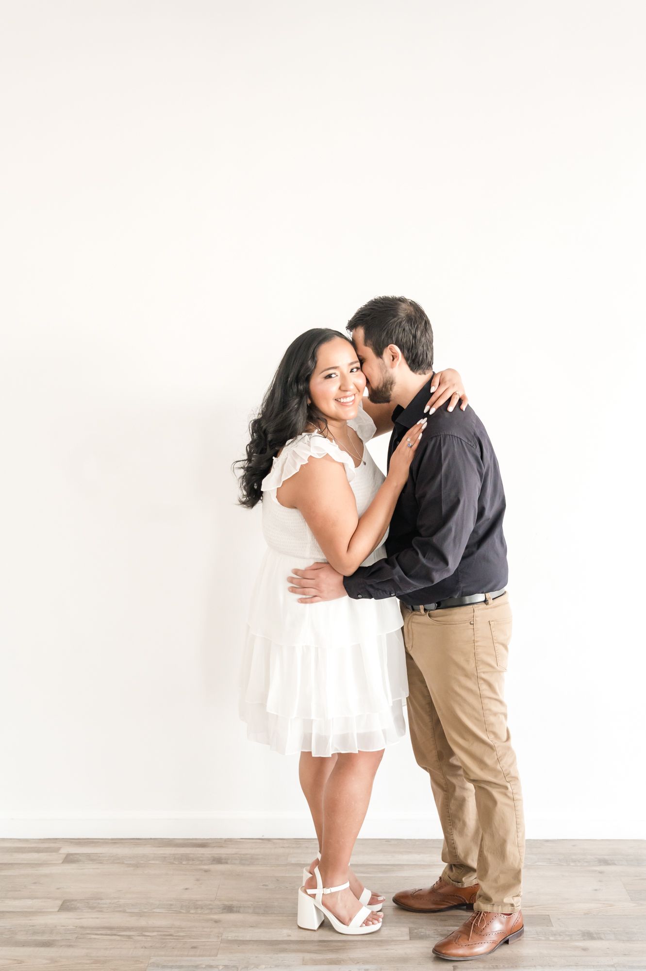 Couple shares tender moment in white and khaki outfits against minimal background.
