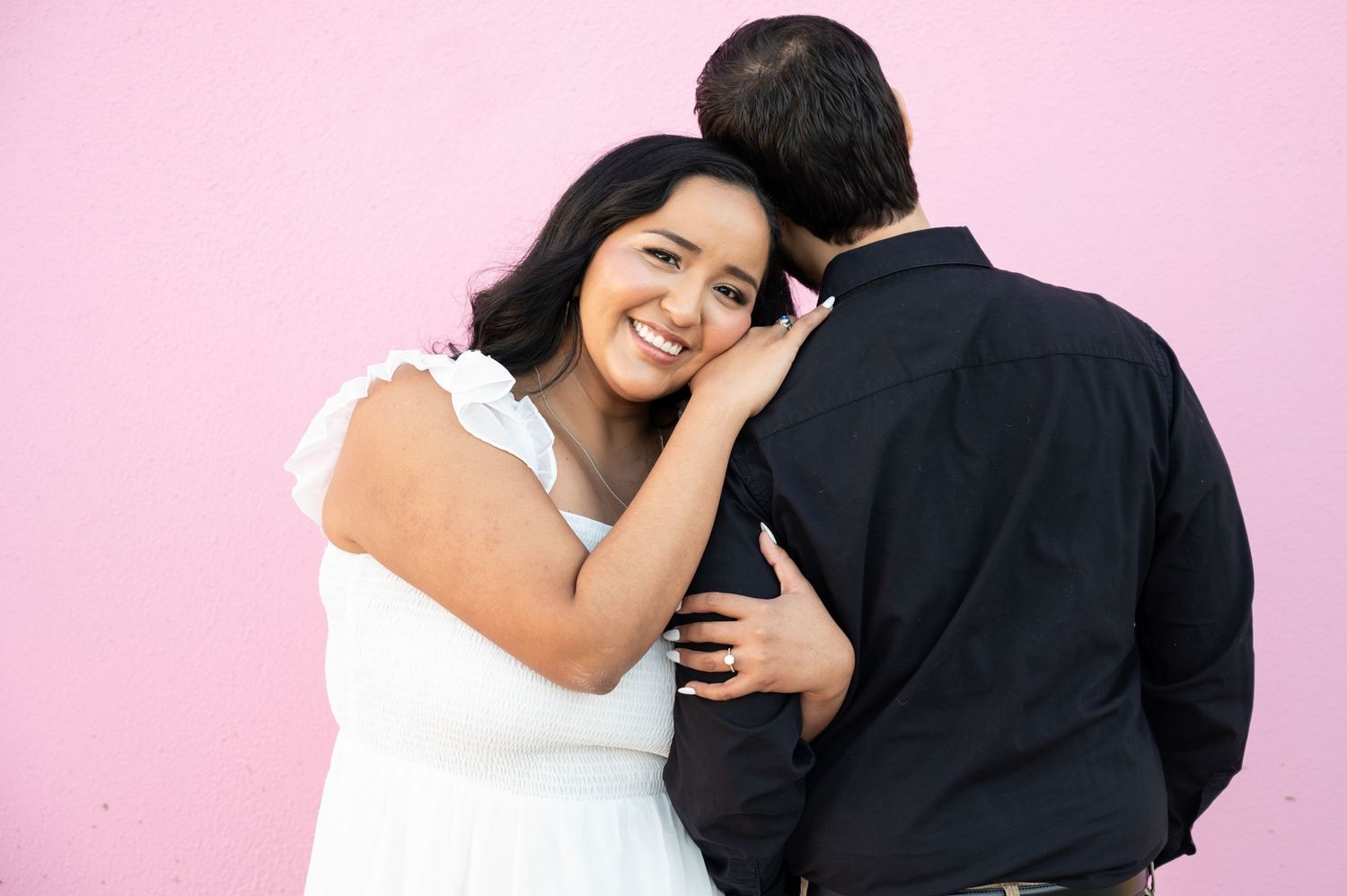 Romantic couple photoshoot against pink background showing tender moments and embraces.