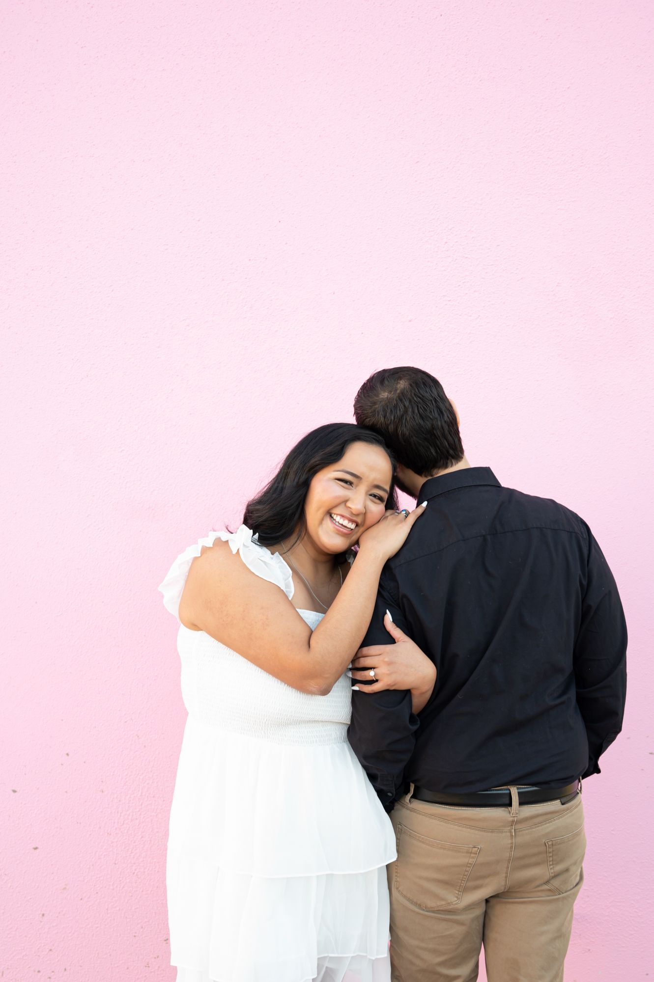 A joyful couple sharing a laugh against a pink wall during their photo session.