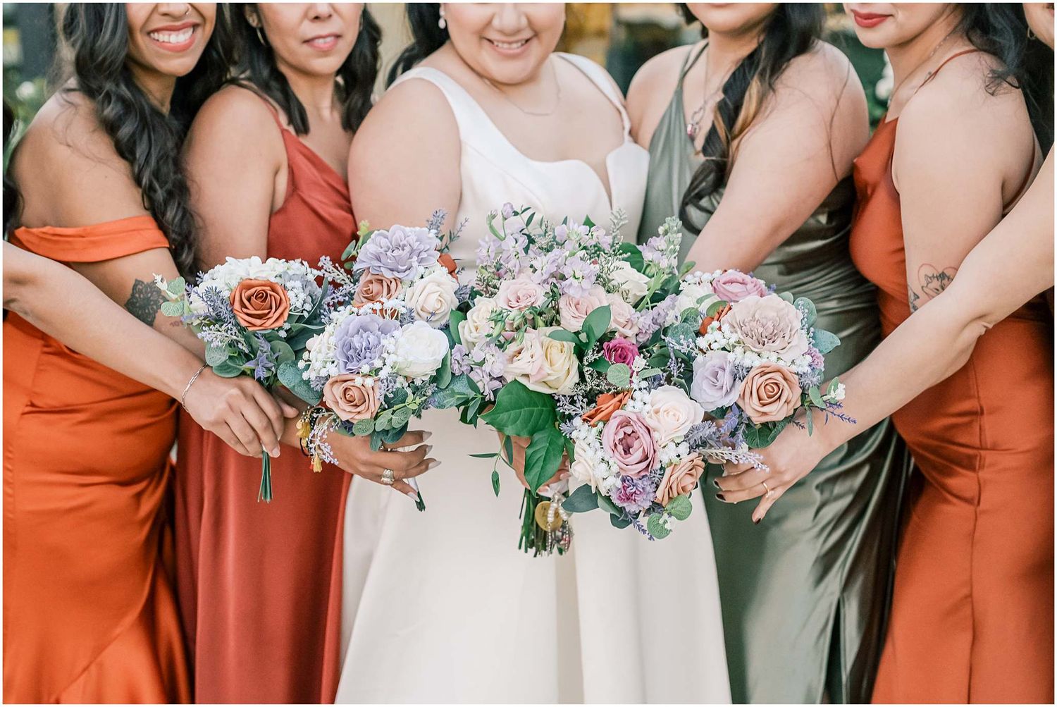 Wedding party members holding pastel floral bouquets in rust and white colored dresses.