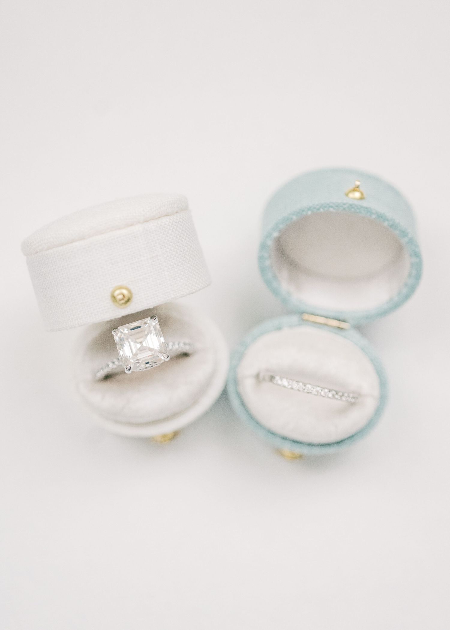 Elegant emerald-cut diamond engagement ring and wedding band displayed in open velvet ring boxes on white background.