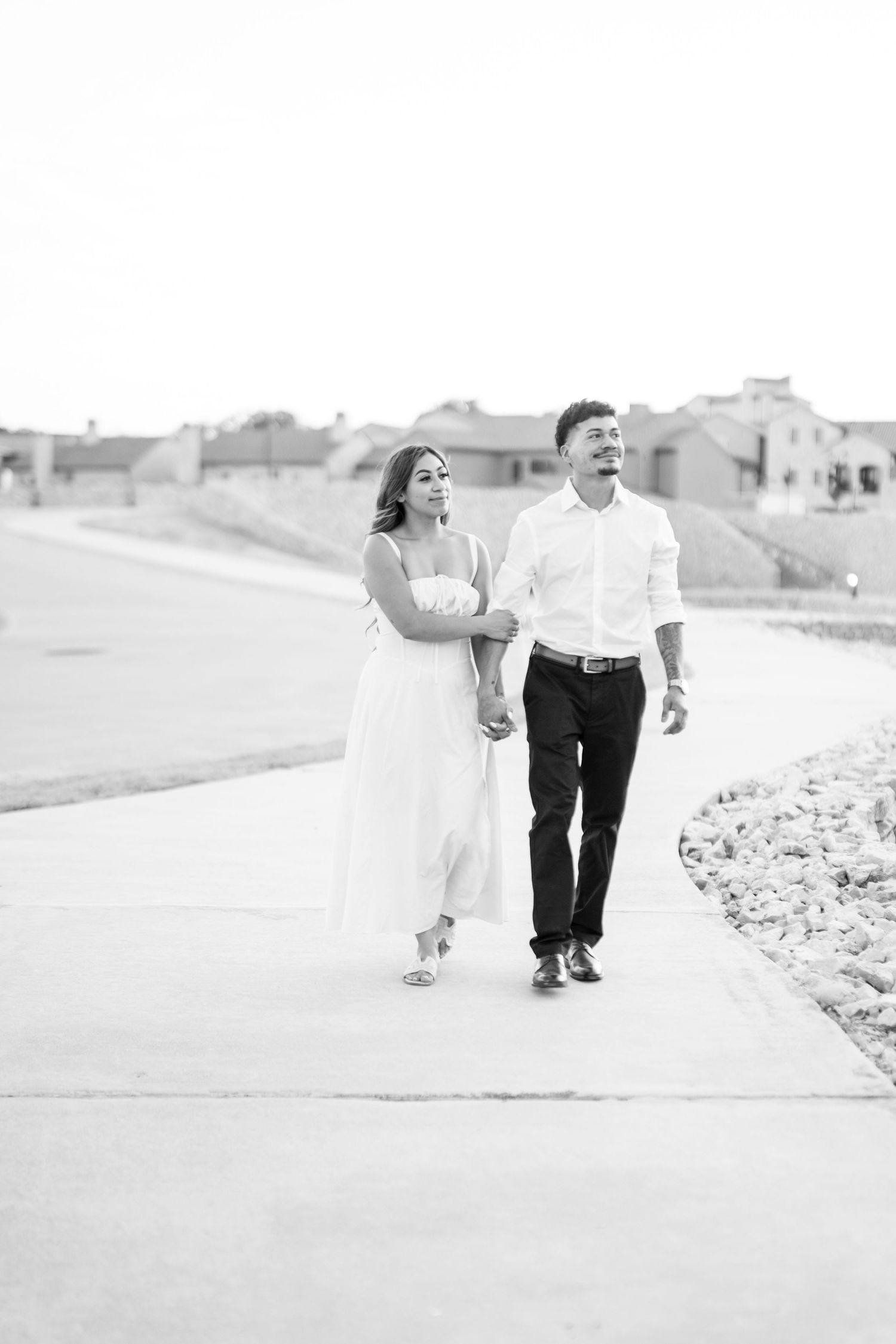 Black and white photo of a laughing couple holding hands and walking along a suburban pathway.