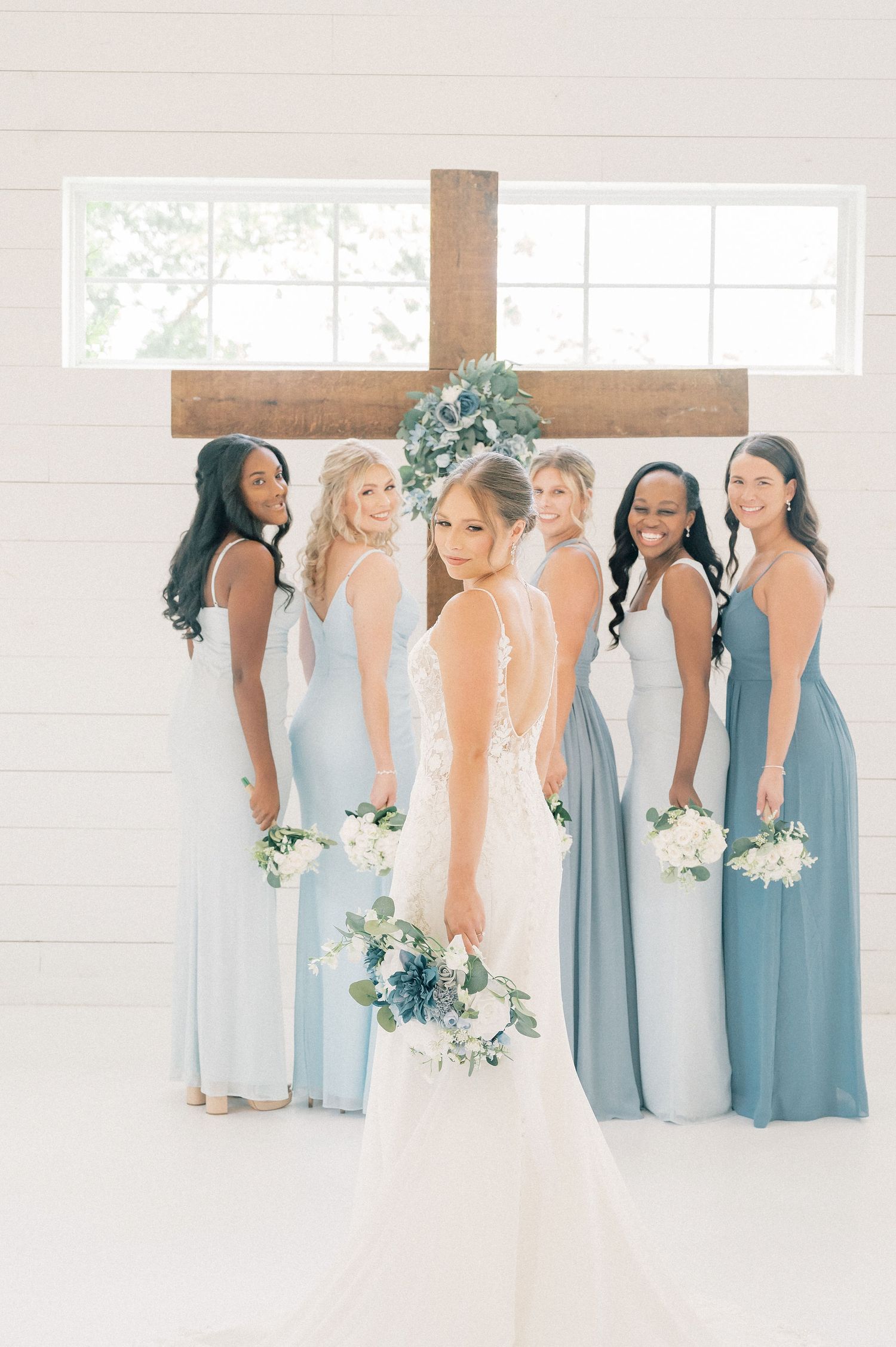 Wedding party in coordinated light blue dresses standing in a bright, airy venue.