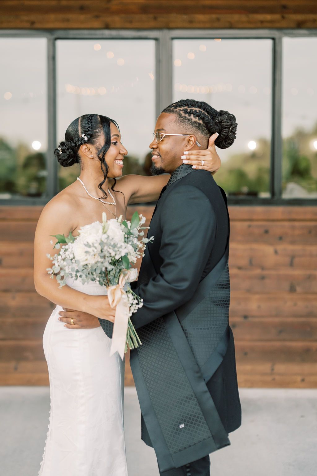 A bride and groom share a romantic embrace, smiling at each other, as she holds a white bouquet at their wedding.