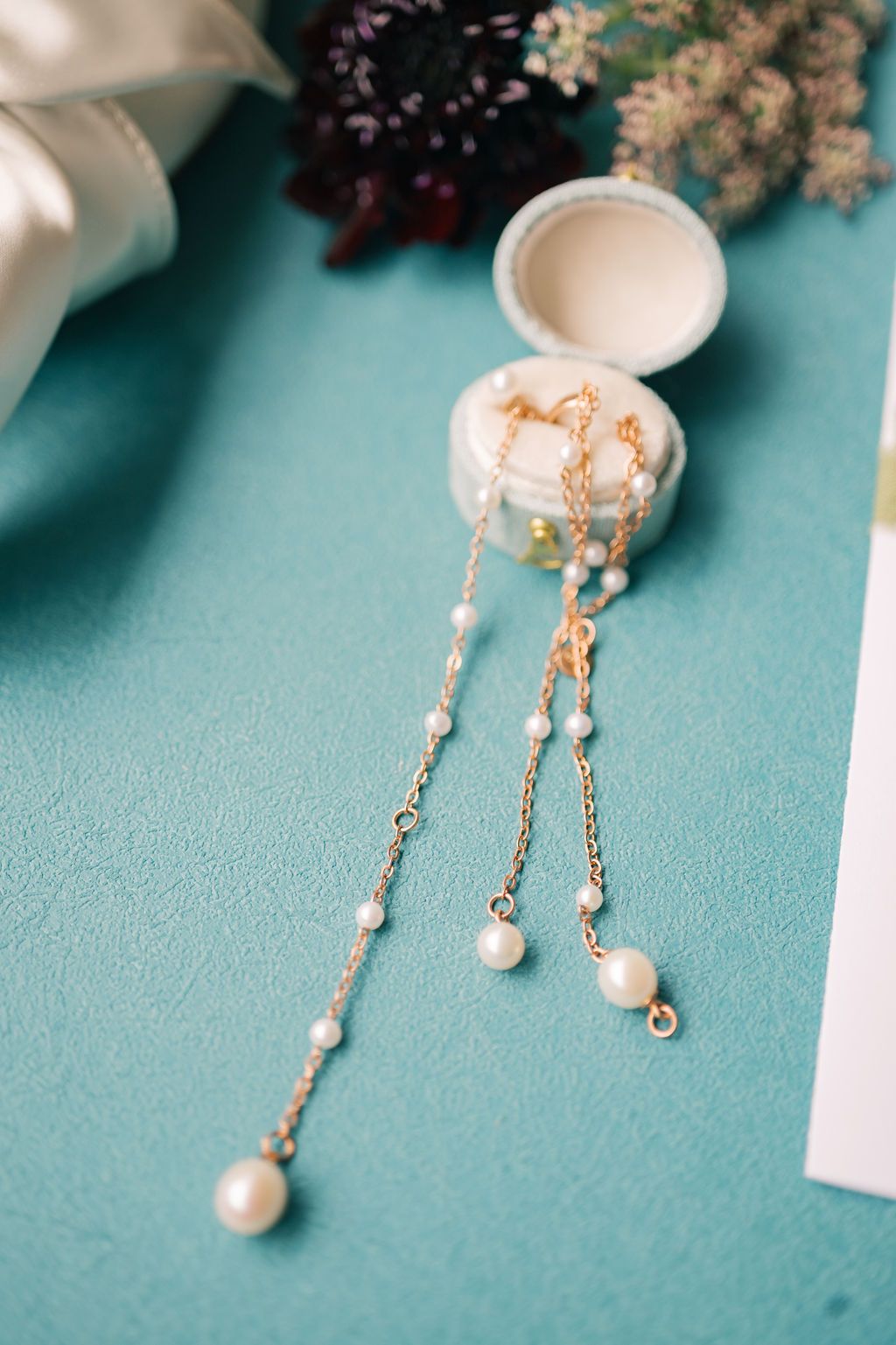 Elegant gold chain drop earrings with pearl accents displayed on a teal surface beside a white jewelry box.