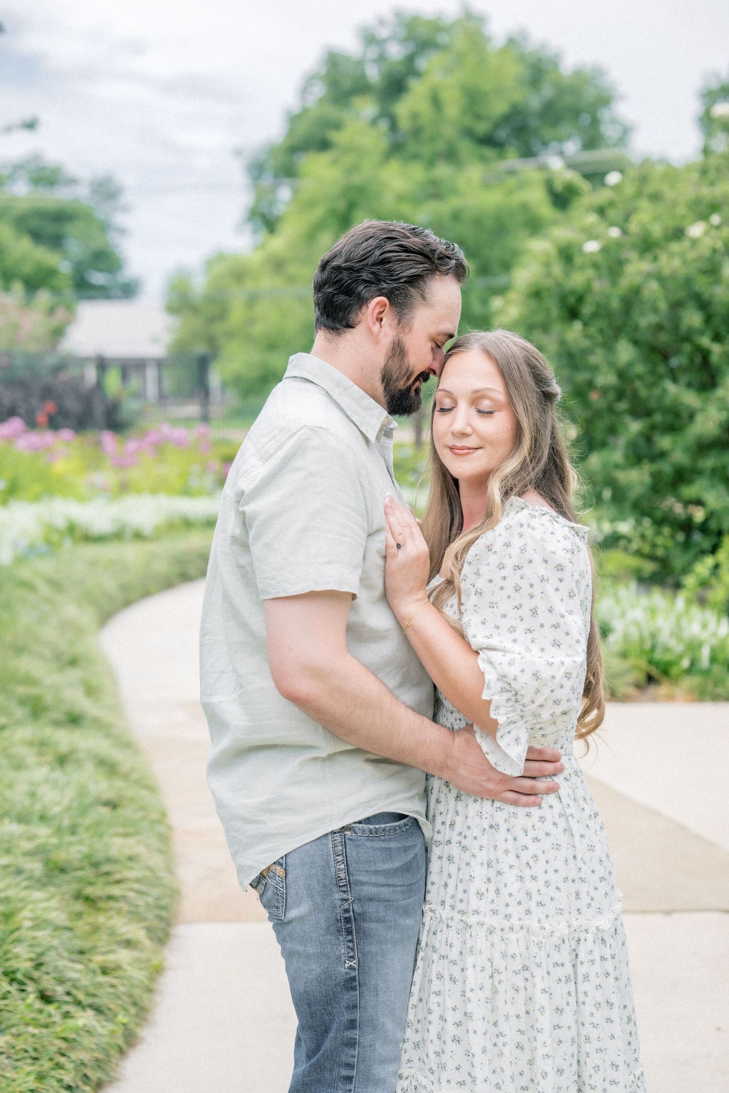 Couple embracing tenderly on a garden path surrounded by lush greenery and colorful flowers.