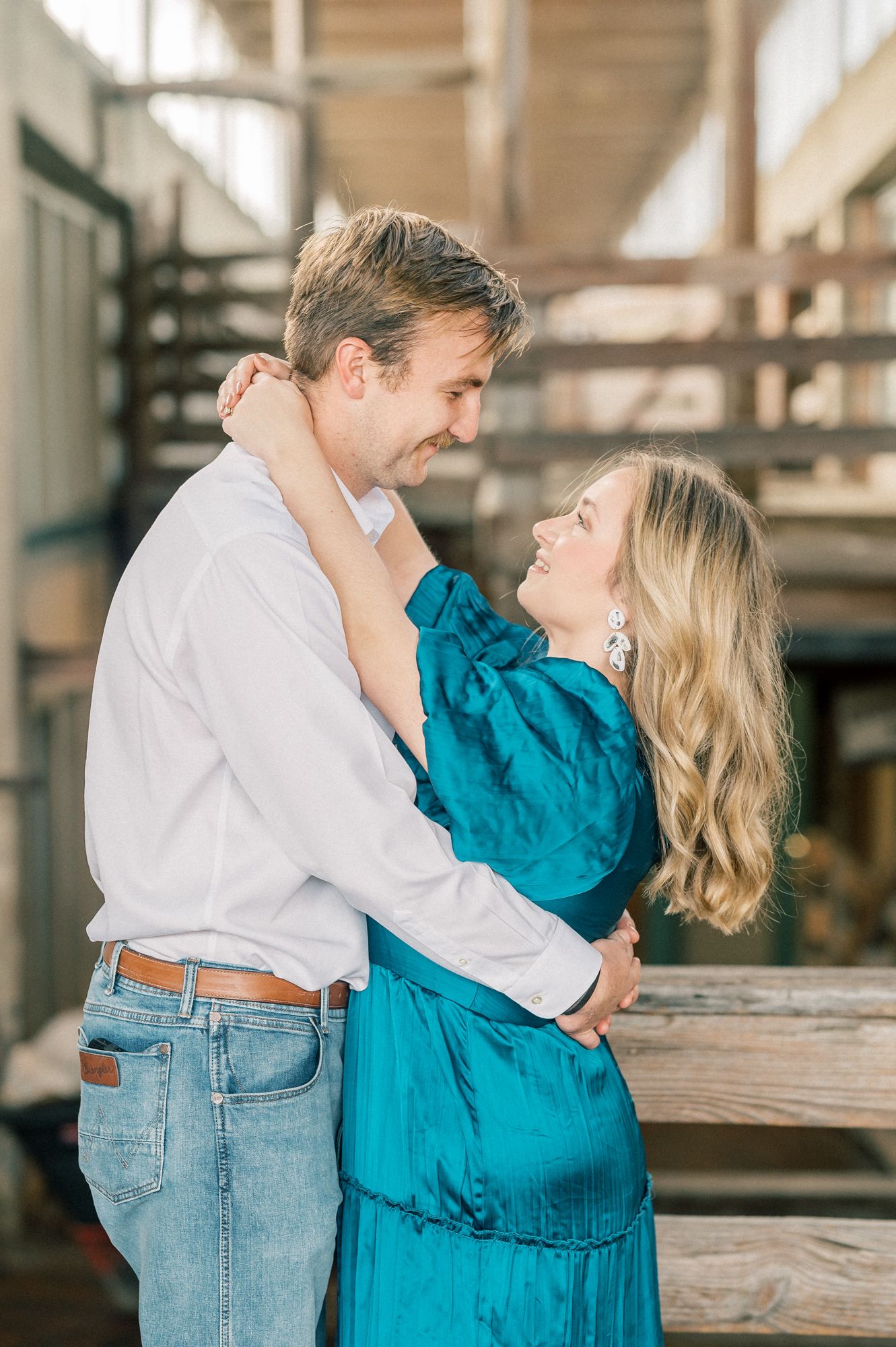 Couple embracing against wooden railing in an industrial-style indoor space wearing blue and white.
