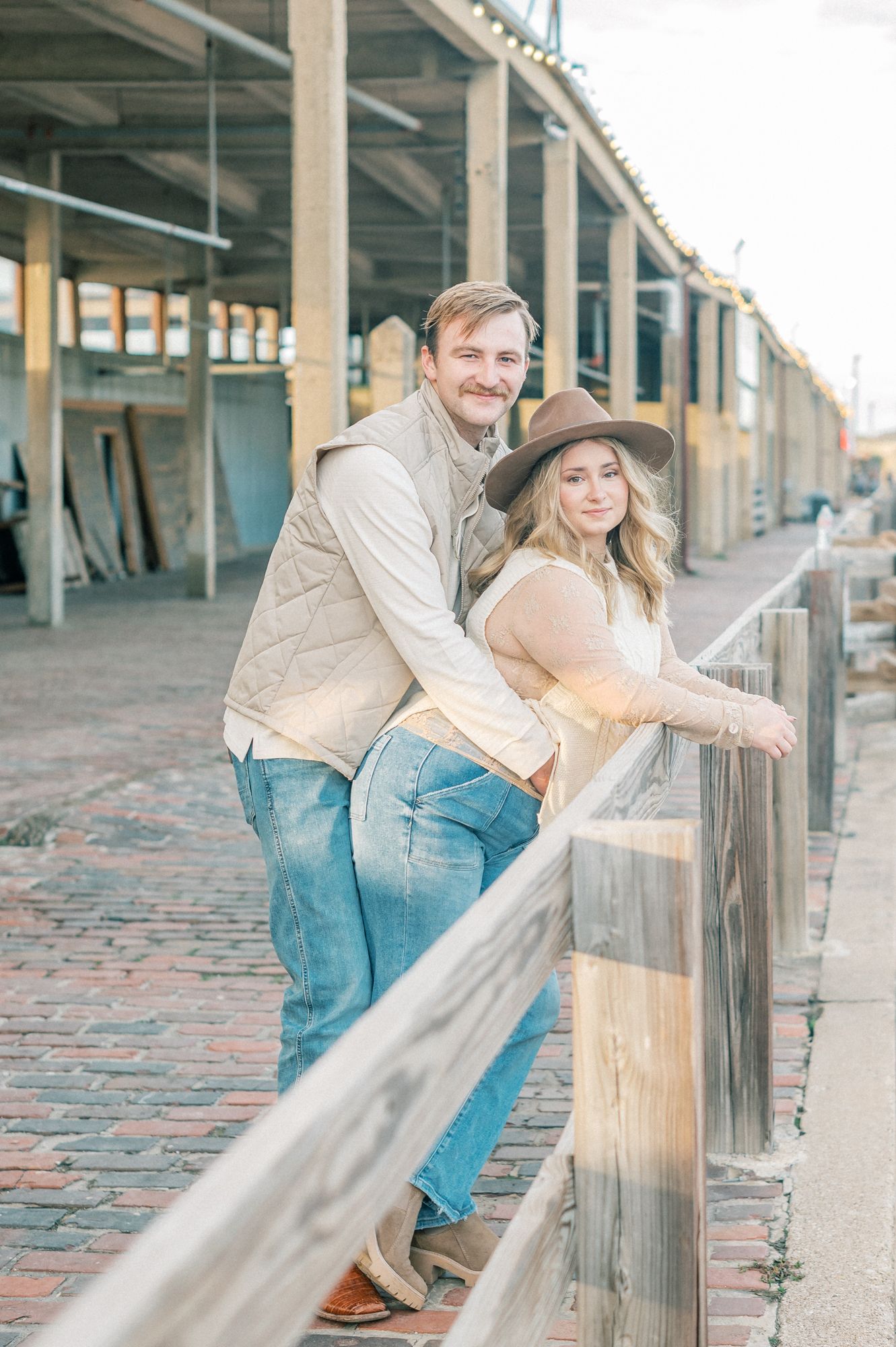 Couple in casual attire sharing playful moments along a brick walkway with columns in an industrial setting.