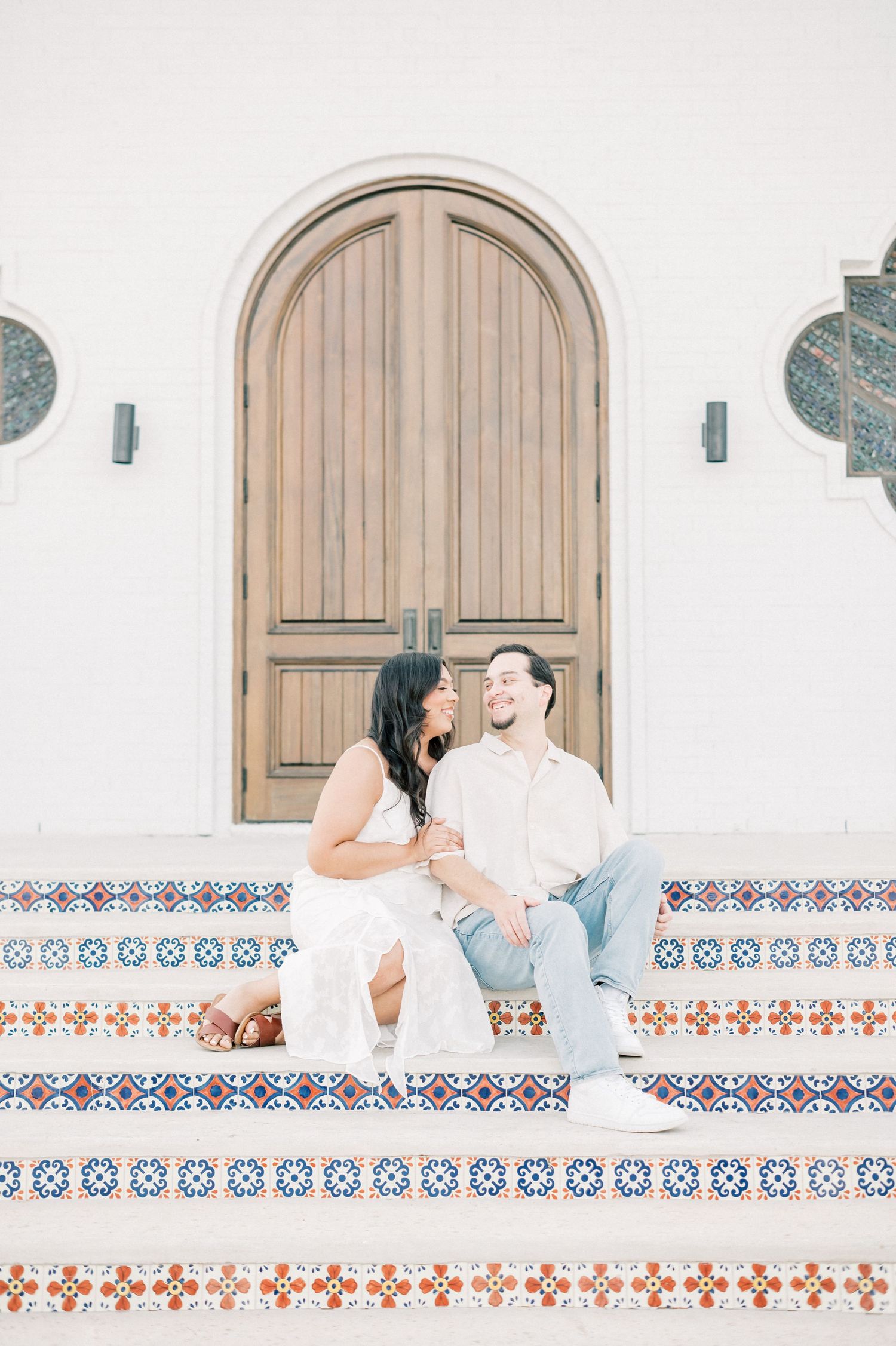 A couple sits on a white bench against a decorative tiled wall with geometric patterns during a romantic photoshoot.