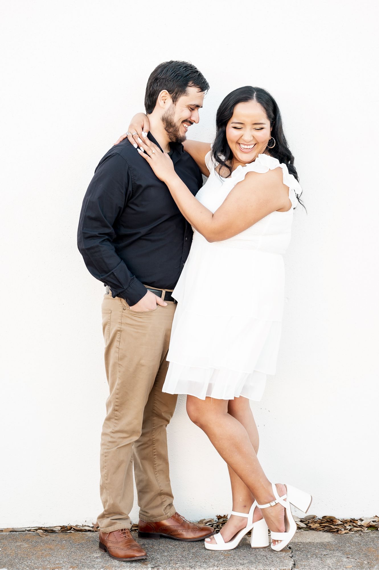 A romantic couple in contrasting black and white outfits share a joyful moment against a white wall.