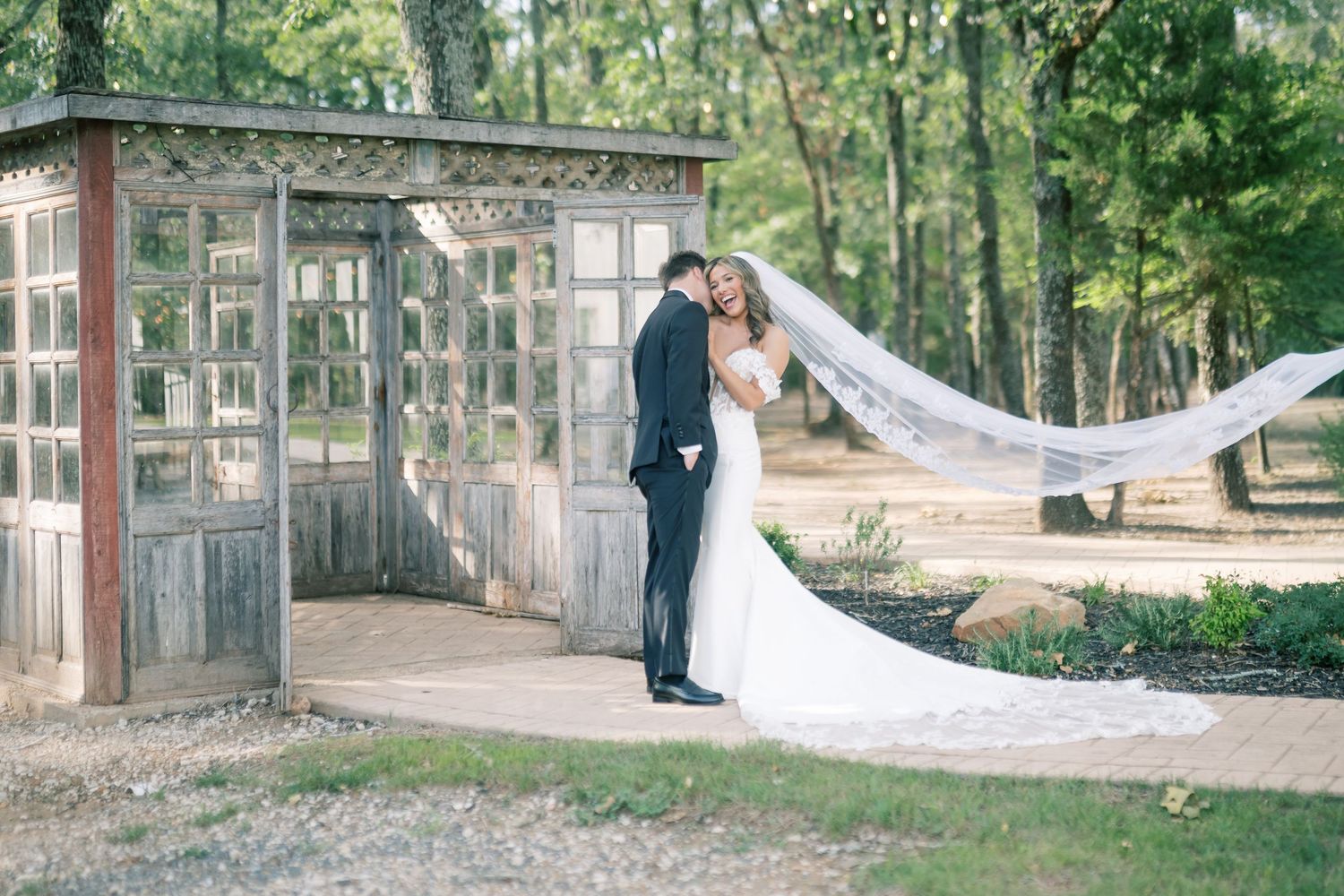Bride and groom embrace outdoors with long veil flowing in the breeze.