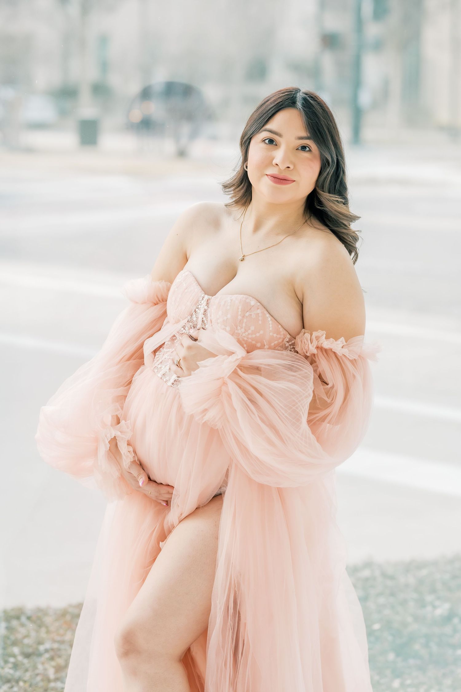 Pregnant woman in pink tulle maternity gown posing outdoors for a maternity photo session.