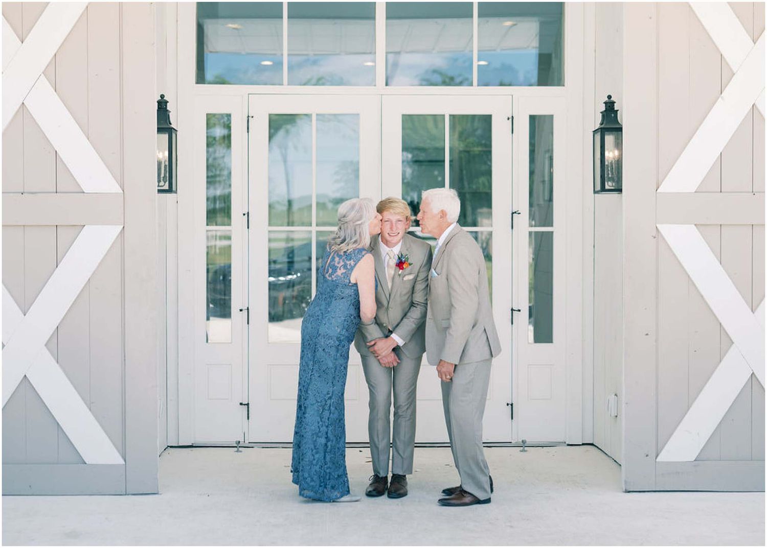 Elderly couple sharing a tender kiss outside white barn wedding venue doors.