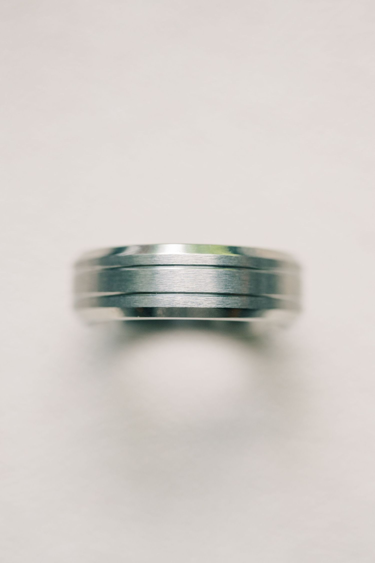 Silver men's wedding band with grooved design displayed on a white surface.