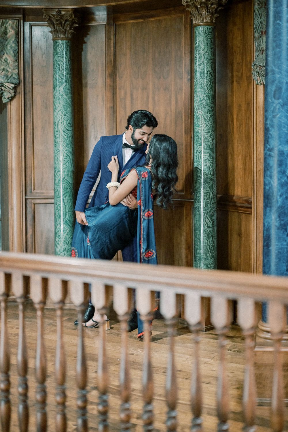 Couple in formal wear shares romantic moment between ornate wooden pillars.
