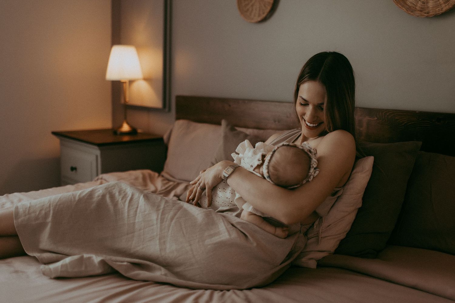 A mother tenderly cradles her newborn baby while relaxing on a bed in a softly lit bedroom.