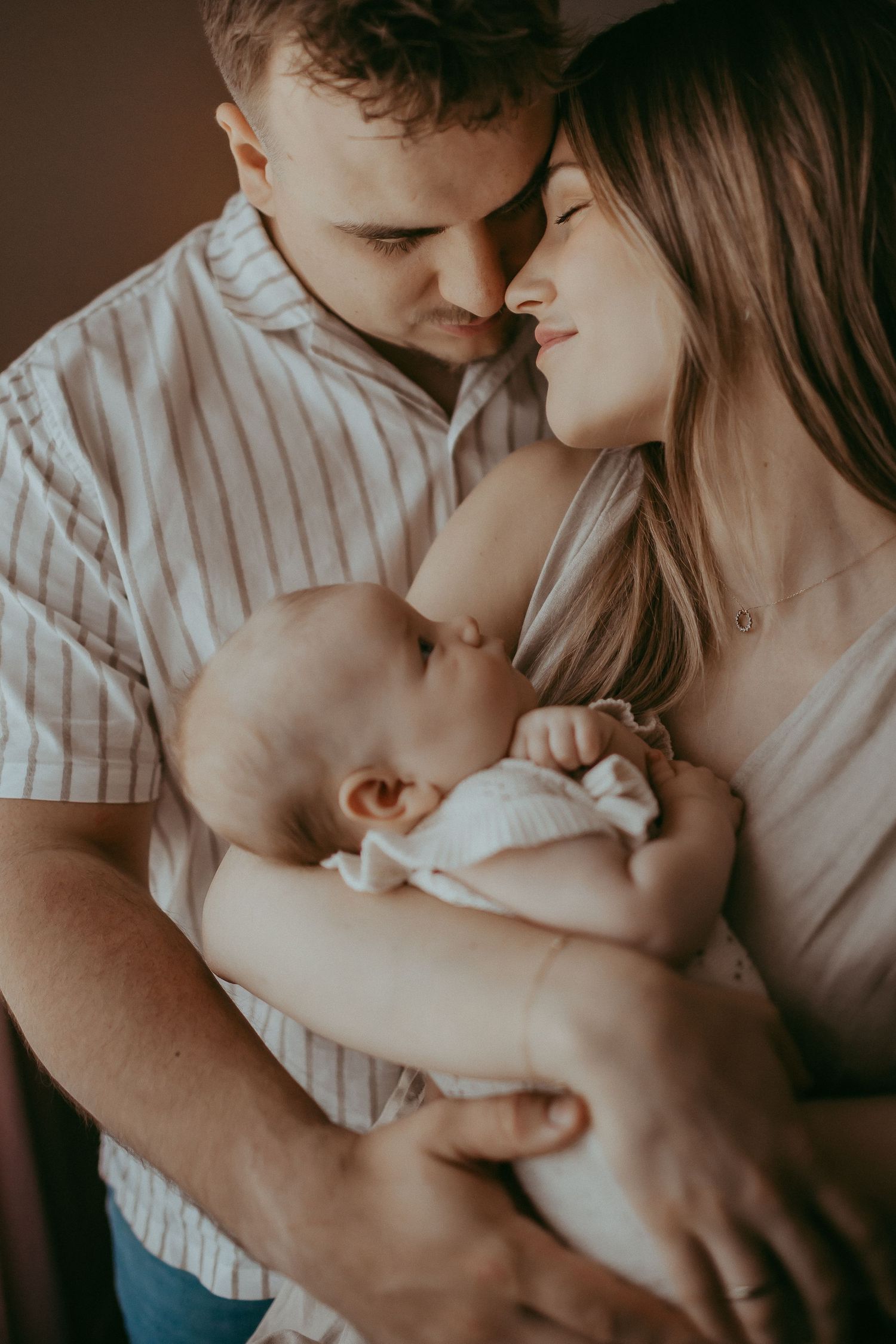 Young parents sharing a tender moment, gently holding their newborn baby together in a warm, intimate embrace.