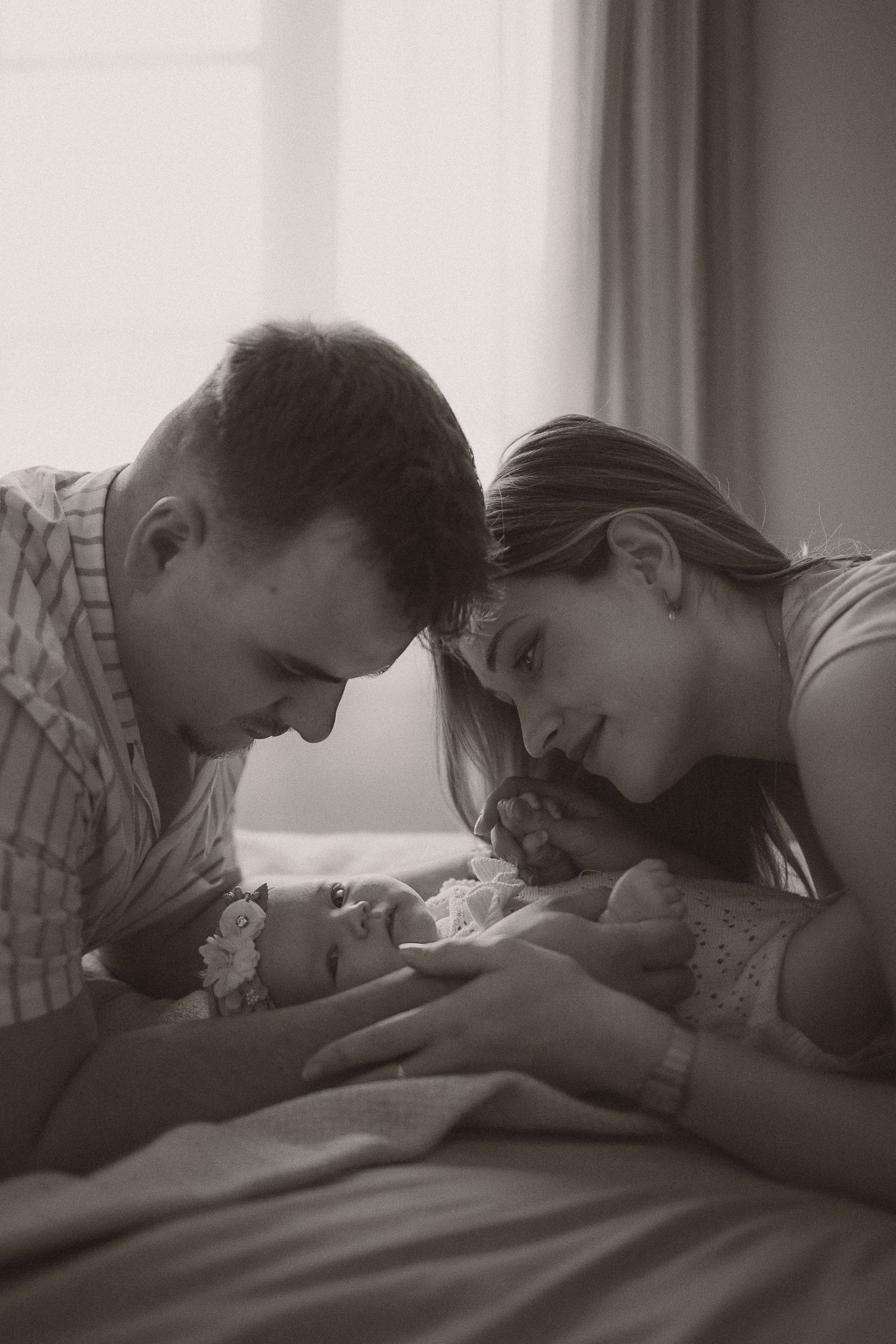 Black and white photo of new parents lovingly gazing at their newborn baby together indoors.