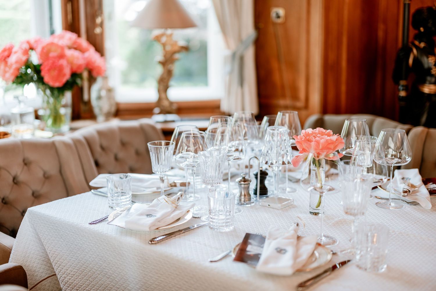 Elegant restaurant table set with crystal glasses, white linens, and pink roses in a warmly lit dining room.