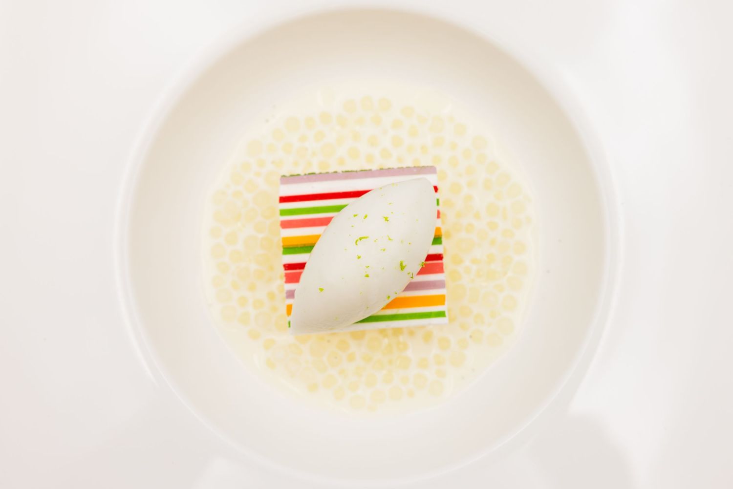 Elegant plated dessert with colorful striped cake slice and white chocolate garnish on a white ceramic plate.
