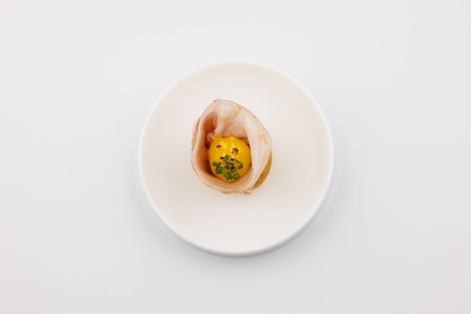 Elegant gourmet appetizer served in a clam shell on a white ceramic plate, featuring vibrant yellow and green filling.
