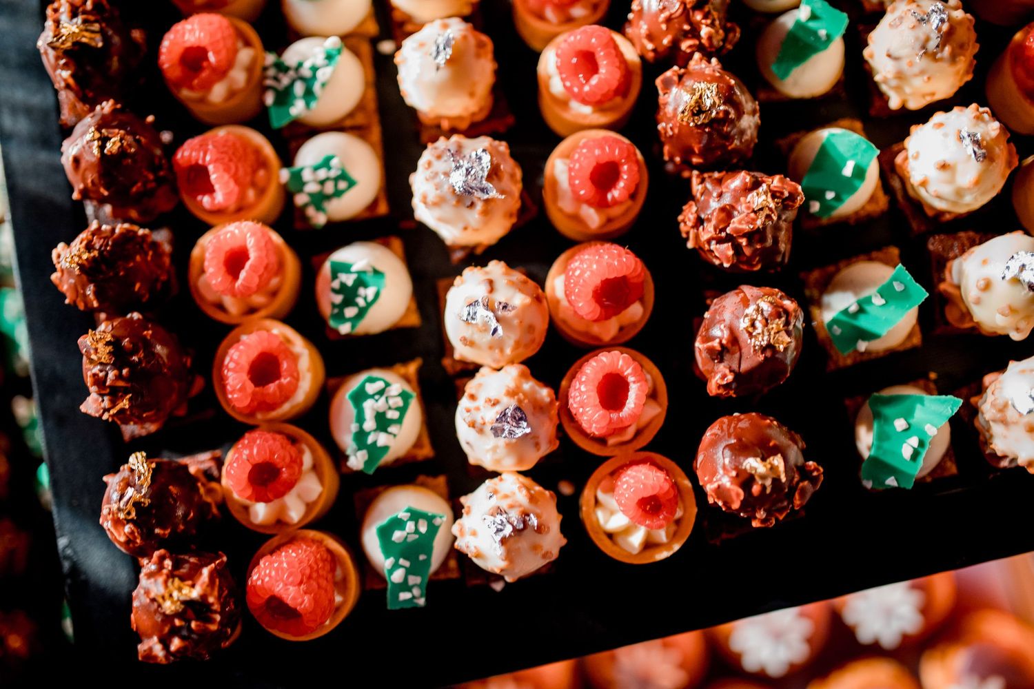 Assorted colorful mini desserts and pastries displayed on a tray, featuring raspberries, chocolate, and festive decorations.