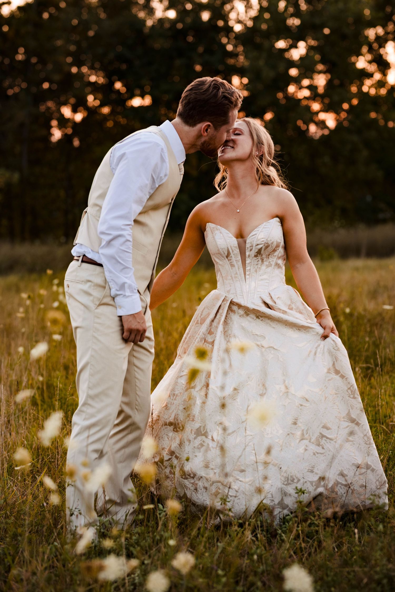 A couple dances together in a golden field at sunset with the bride's white dress flowing in the wind.