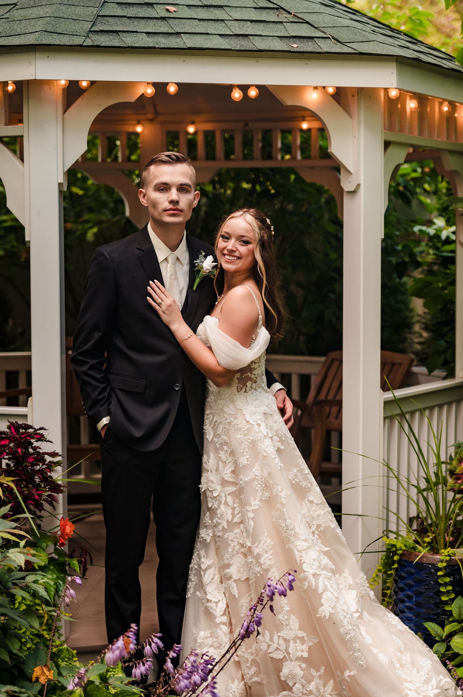 A couple poses playfully by a white garden gazebo with floral decorations.