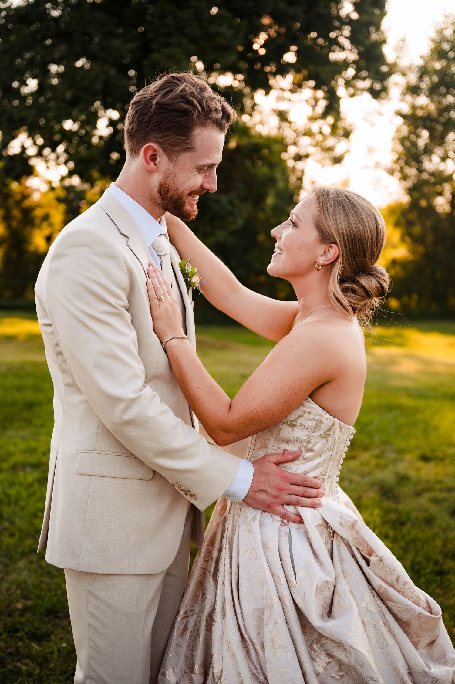 Joyful couple embracing in golden sunset light wearing cream and champagne formal attire.