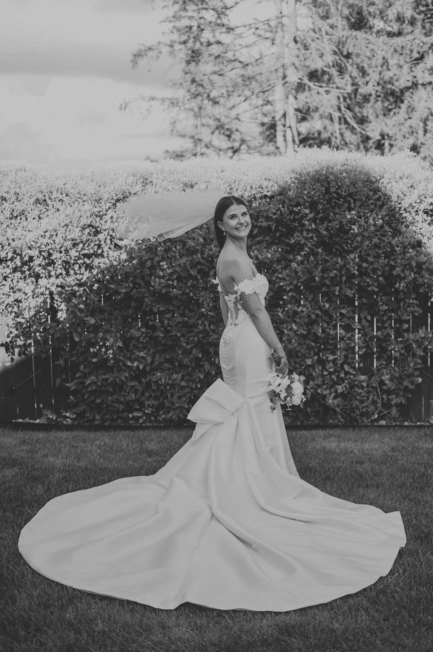Black and white bridal portrait showcasing dramatic train of mermaid wedding gown in garden setting.
