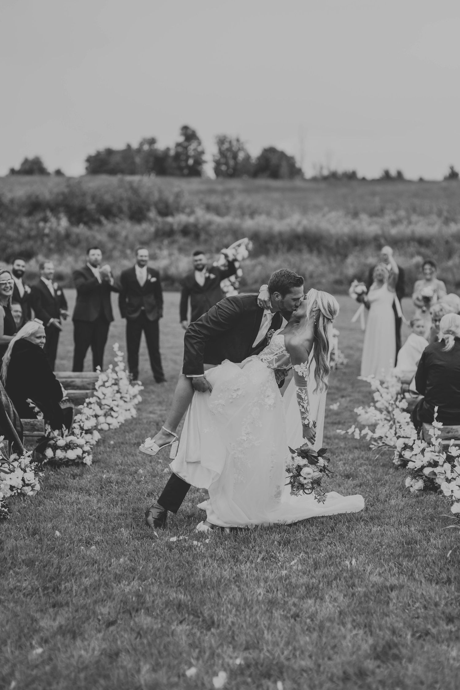 Black and white photo captures romantic dip kiss between newlyweds during outdoor ceremony.