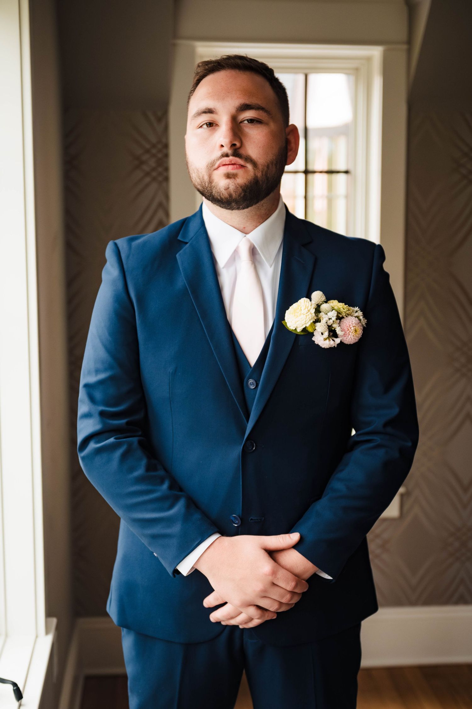 Groomsmen in navy blue suits with boutonnieres stand in formal indoor setting.